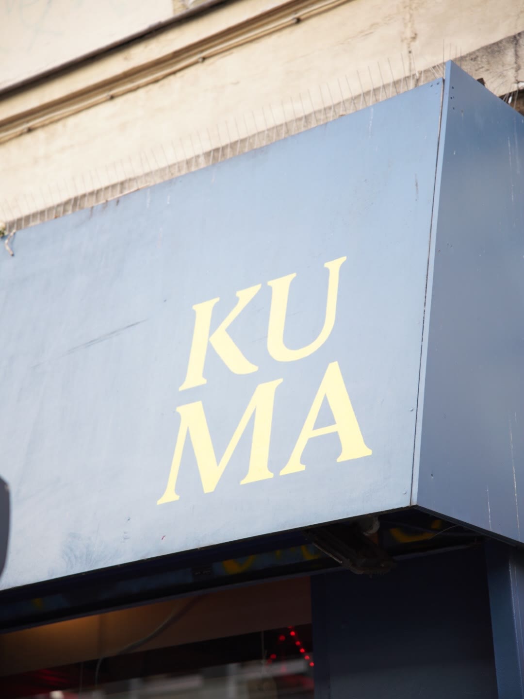 Enseigne KUMA en lettres jaunes sur la façade bleu gris, vue rapprochée